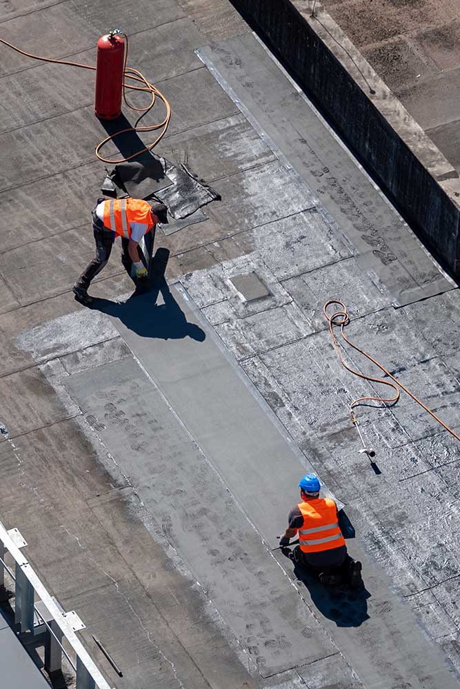 Vogelperspektive einer Dachbaustelle. Professionelle Bitumenabdichtung an einem Flachbau